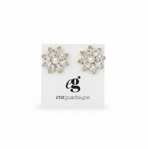 A pair of silver-toned floral stud earrings displayed on a white card inside an open blush pink velvet jewelry box, held by a hand in a busy retail setting.